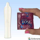 A person with pink nail polish holds a purple "Caution Wear 'Wild Rose'" ribbed condom package. Beside it is an unwrapped condom, showcasing its textured design. The Condomania logo is prominently displayed in the corner, set against a gradient of blue and white.
